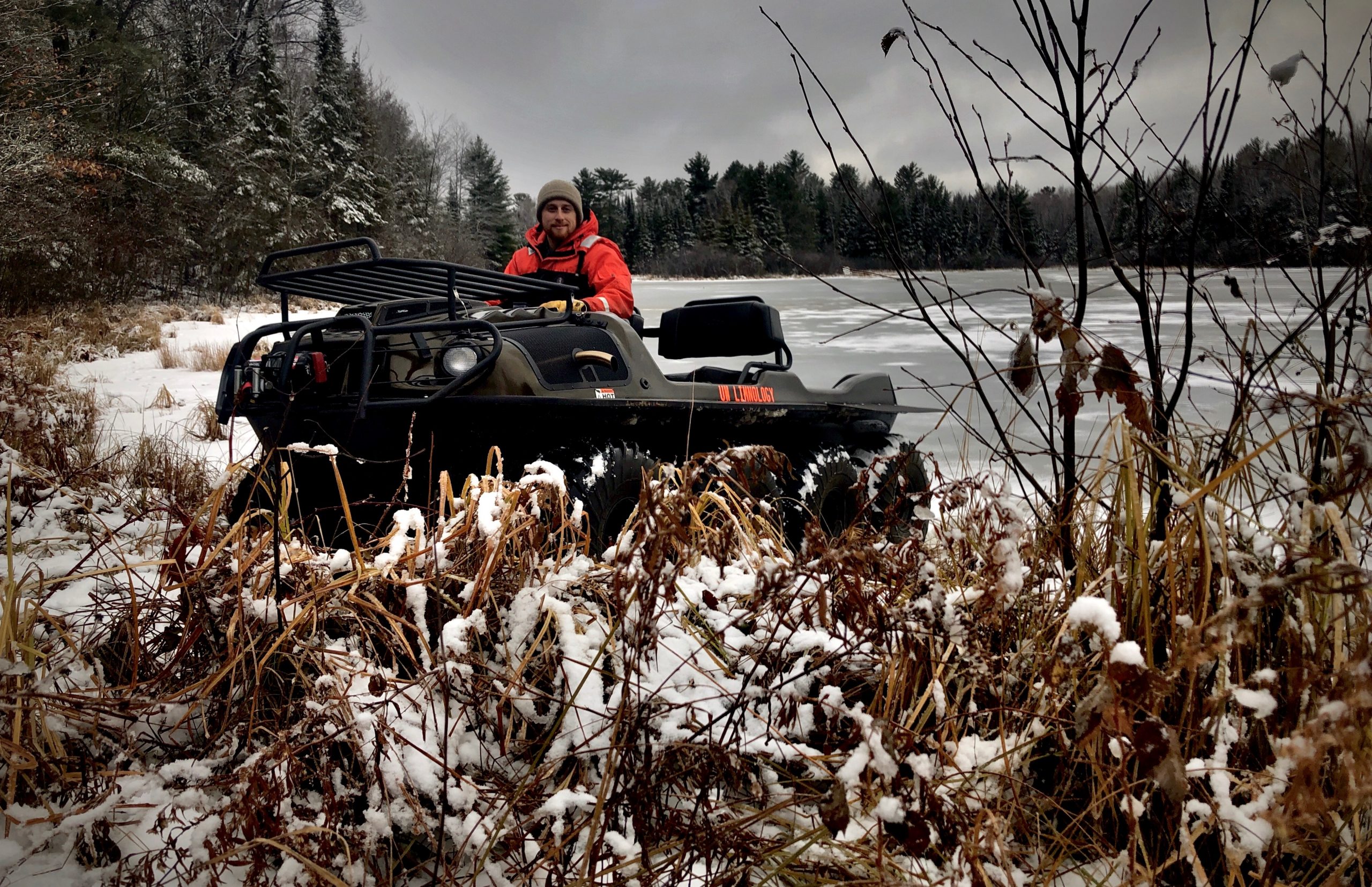 Person is driving ATV off lake ice onto shore in snow