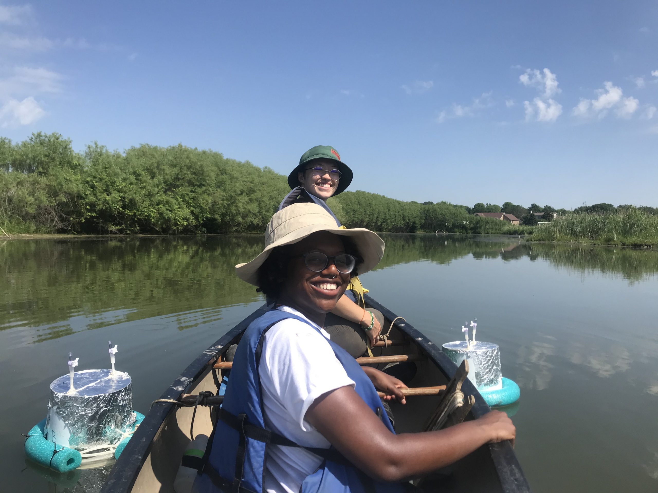Two people looking back at camera from front of canoe on lake with lakeshore in background