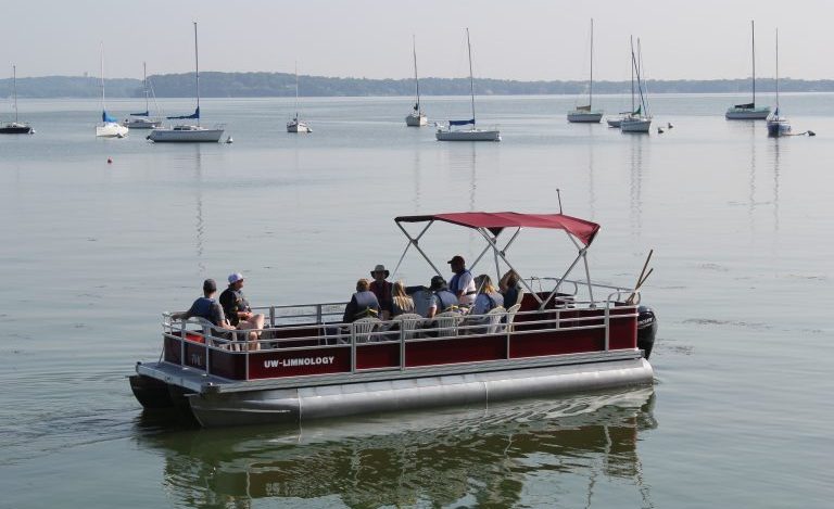 Open House participants riding CFL pontoon boat on Lake Mendota with sail boats in background