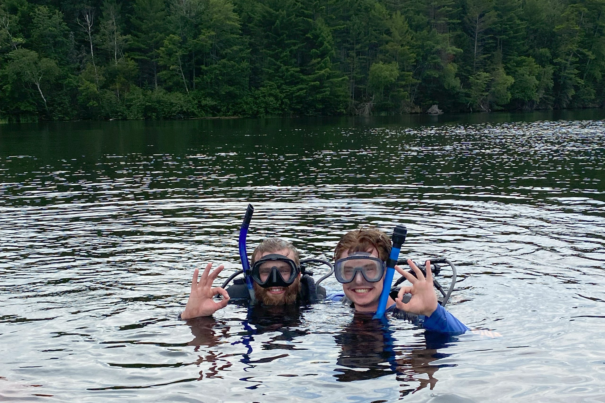 There are two people in SCUBE gear with their heads above water giving a thumbs up to the camera